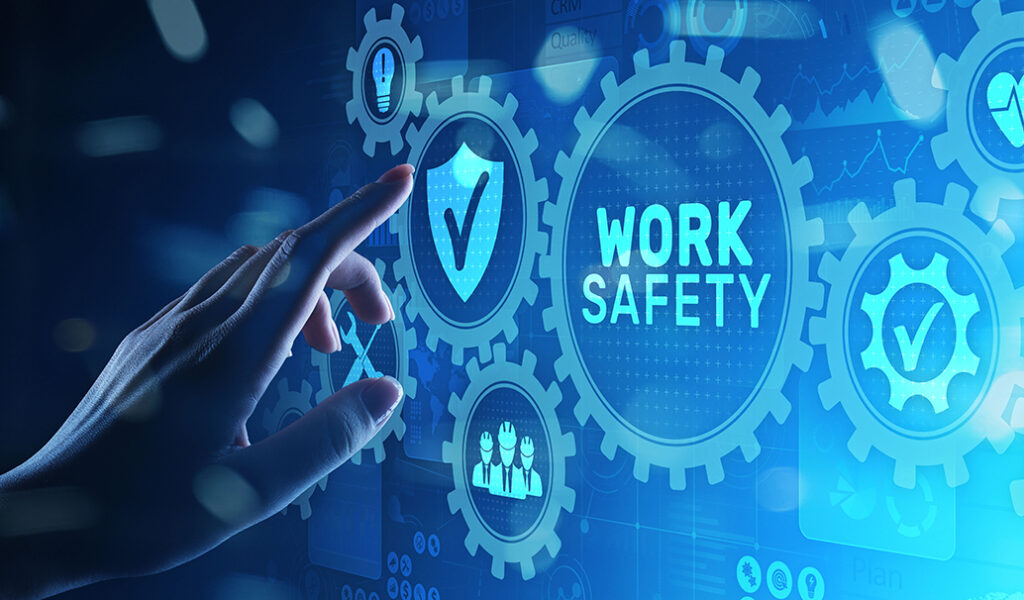 A hand is reaching toward virtual gears displaying icons and text, including a shield, people, and the words WORK SAFETY, symbolizing workplace safety and protection in a digital, high-tech style.
